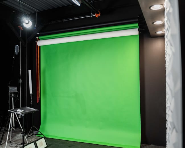 A photography studio featuring a large green backdrop and various lighting equipment.