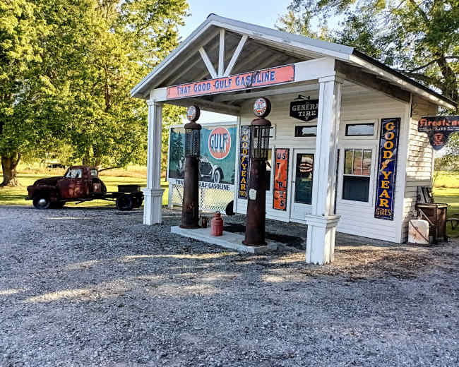 The image shows a vintage gas station with two old-fashioned fuel pumps and a classic truck parked nearby.