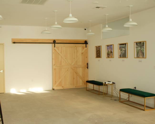 The image shows a minimalist interior space featuring a wooden sliding barn door, two framed artworks on the wall, and a seating area with green cushions and a projector.