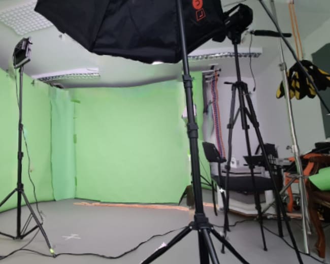 A photography studio set up with green backdrop screens and various light stands.