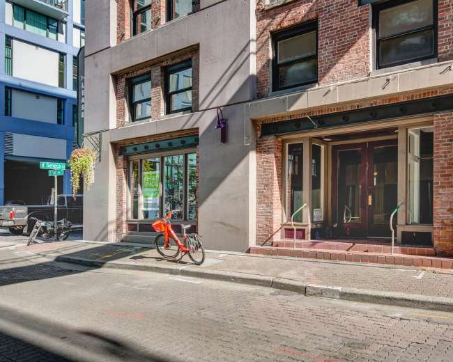 The image shows a brick building with large display windows on a quiet street, where a red bicycle is parked next to the curb.