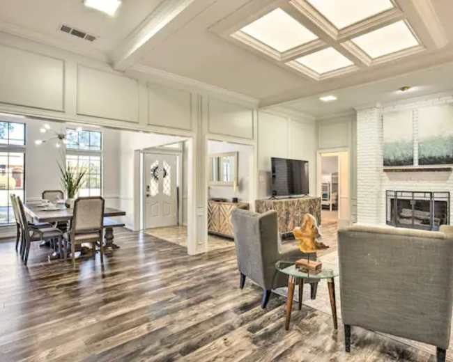 A spacious living area with wooden flooring, a seating area, and an adjacent dining space, featuring large windows and a fireplace.