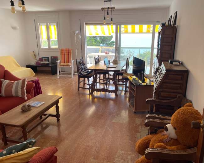 The image shows a partially furnished living room with two sofas, a dining table, and large windows overlooking a view of the outdoors.