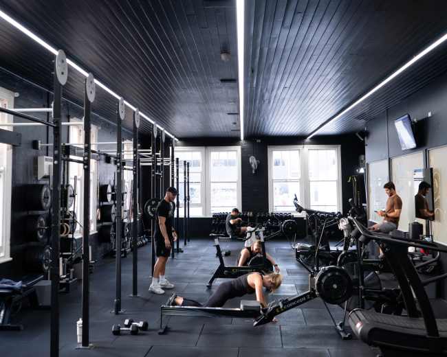 A modern gym with workout equipment and several individuals engaging in various exercises.