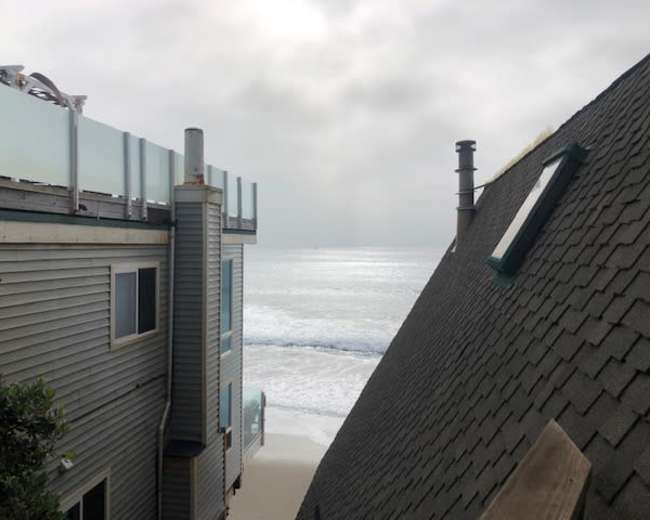 A view of a beach scene with ocean waves visible in the distance, framed by two buildings.