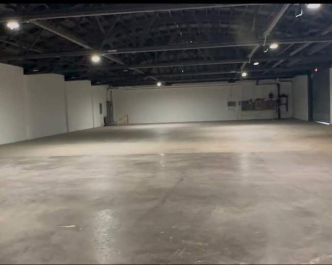 The image shows a spacious, empty industrial room with concrete flooring and white walls.