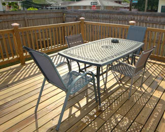 A metal table with four chairs is set on a wooden deck surrounded by a wooden fence.