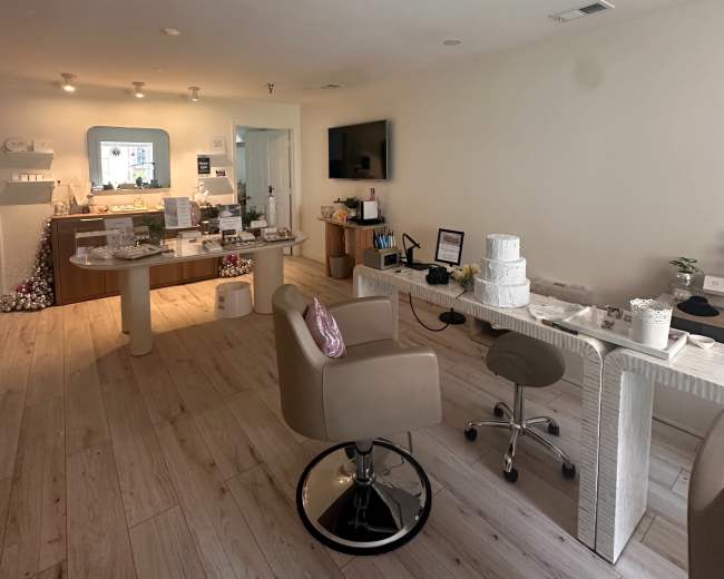 The image shows a modern, well-lit workspace with wooden flooring, featuring a reception area with a desk, a seating area, and various decorative elements.