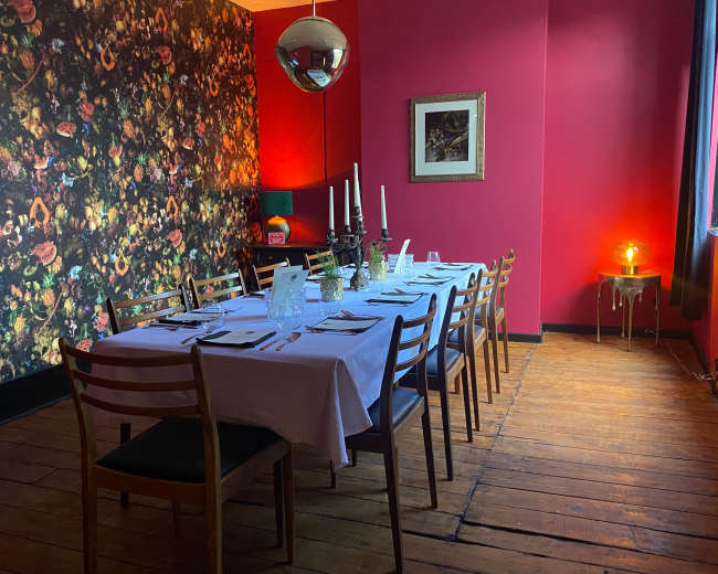 A long dining table is set for a meal in a brightly colored room with floral wallpaper and a large disco ball.