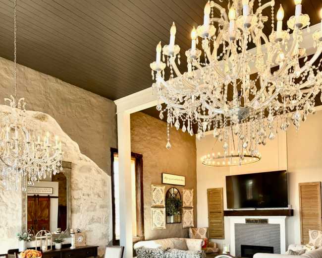 The image shows a modern living and dining area featuring a large kitchen island, multiple chandeliers, and a stylish seating arrangement.