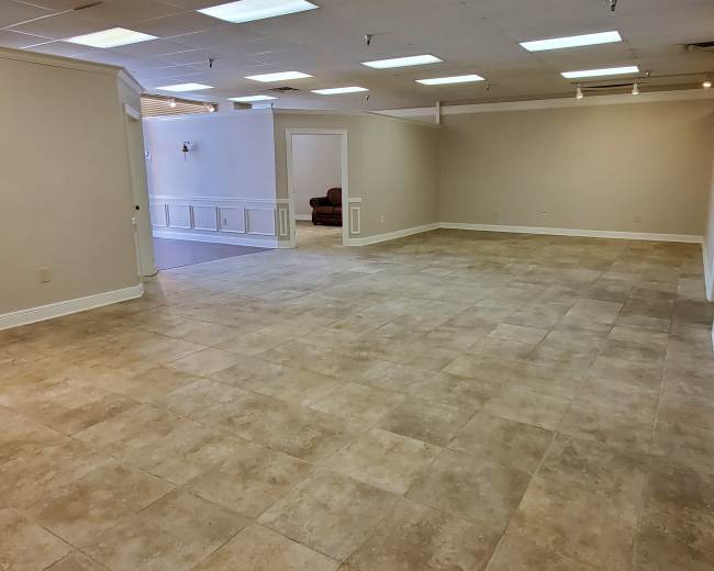 A spacious, empty room with tiled flooring, white walls, and several ceiling lights.