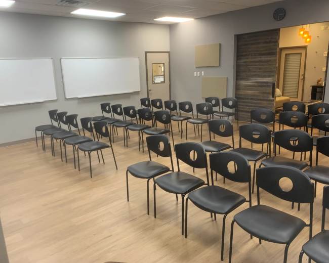A classroom setup with several rows of black chairs arranged in front of whiteboards.