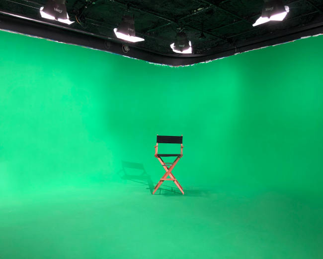 The image shows a green screen studio with a single red director's chair positioned at the center.