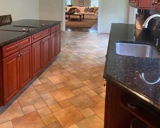 A view from a kitchen featuring wooden cabinetry and a granite countertop, leading into a living room area through an open doorway.