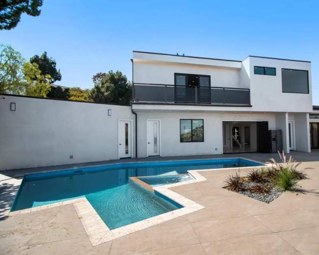 The image shows a modern two-story house with a balcony, a swimming pool, and a landscaped patio area.