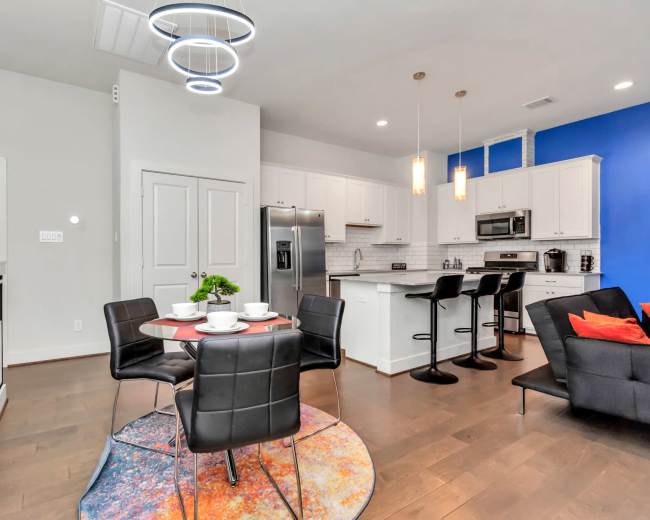 A modern kitchen and dining area feature a round table with black chairs, a stainless steel refrigerator, and a blue accent wall.