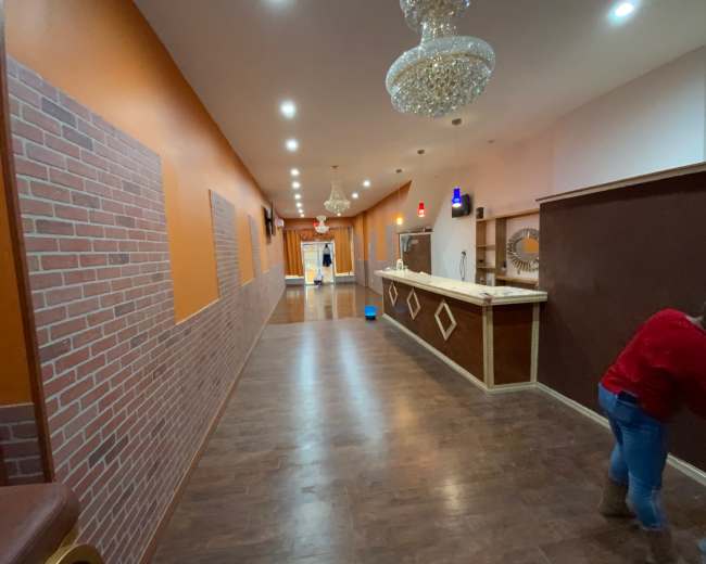 A long, well-lit hallway with wooden flooring, brick-patterned walls on one side, and a counter at the end.