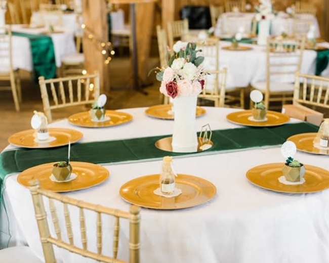 A round dining table is set with gold plates and decorative centerpieces in a venue adorned with wooden accents.