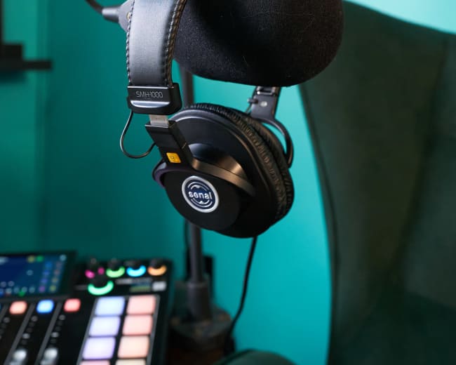A microphone is mounted on a stand next to a pair of headphones in a recording studio with green and blue walls.