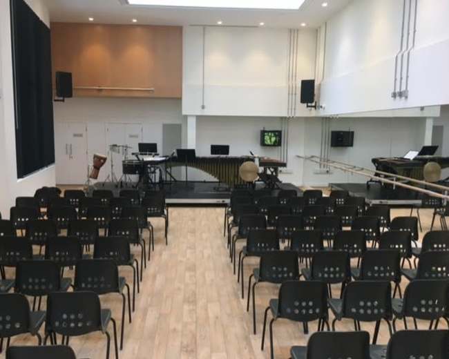 A music performance space with rows of black chairs facing a stage set up with various musical instruments and equipment.