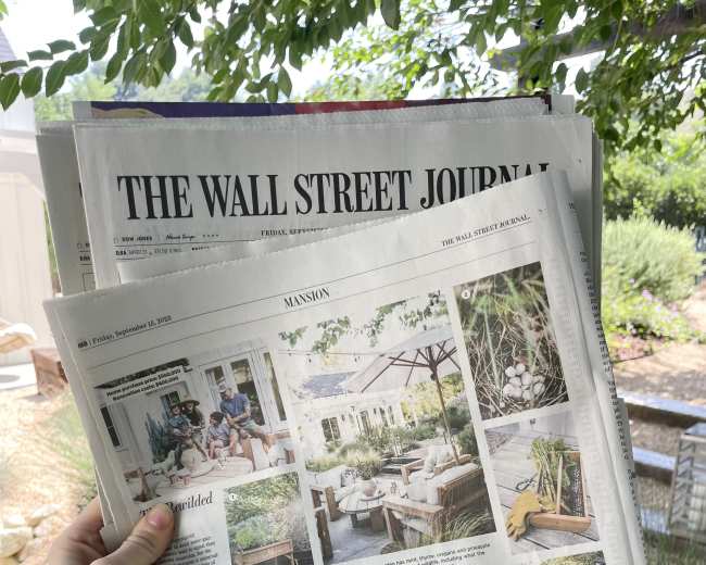 A person holds a copy of The Wall Street Journal featuring a lifestyle section with images of a garden and outdoor seating.