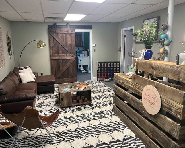 The image shows a cozy basement living area with a brown leather couch, a decorative wooden coffee table, and a wooden partition with various decorative items.