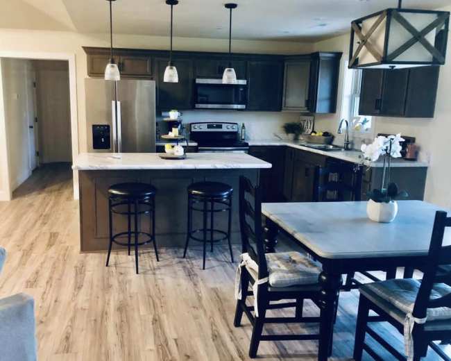 A modern kitchen with dark cabinetry, a large island with seating, and a dining table set for meals.