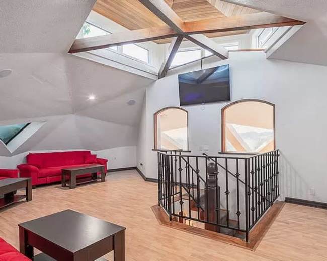 The room features a spacious loft with red sofas, wooden flooring, and large windows allowing natural light to enter.