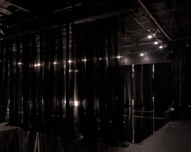 The image shows a dimly lit space with black sheer curtains hanging, creating an atmosphere of separation within the room.