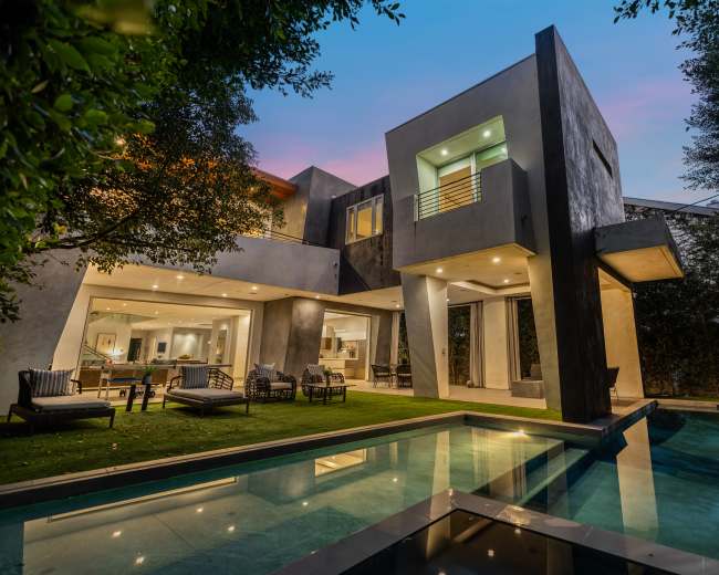 The image shows a modern house with a swimming pool, surrounded by greenery, and features large glass windows and a contemporary design.