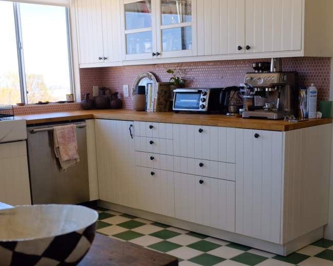 A bright kitchen features white cabinets, a tiled green and white floor, and a countertop with various appliances.