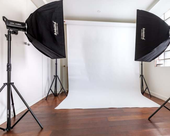 The image shows a photography studio setup with a white backdrop and two softbox lights positioned on either side.