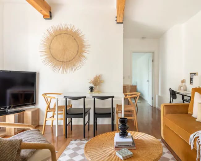 The image shows a modern living space with a cozy brown sofa, a round coffee table, a dining area with a black table and chairs, and decorative wall elements.