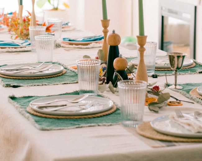 A dining table is set with plates, glasses, cutlery, and decorative candles in a bright, modern room.