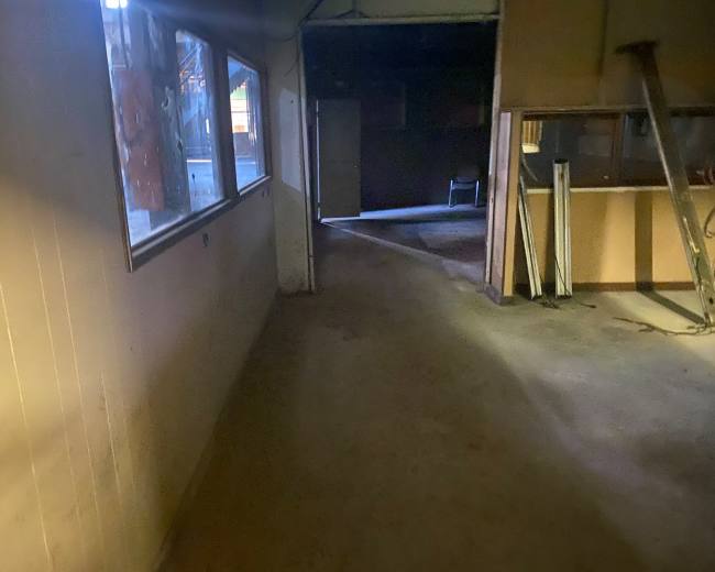 The image shows a dimly lit hallway in an empty, unadorned building with visible windows on one side.