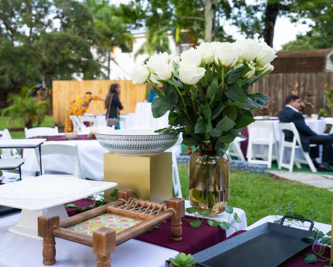 A decorated outdoor setting with white tables, floral arrangements, and various serving trays arranged for an event.