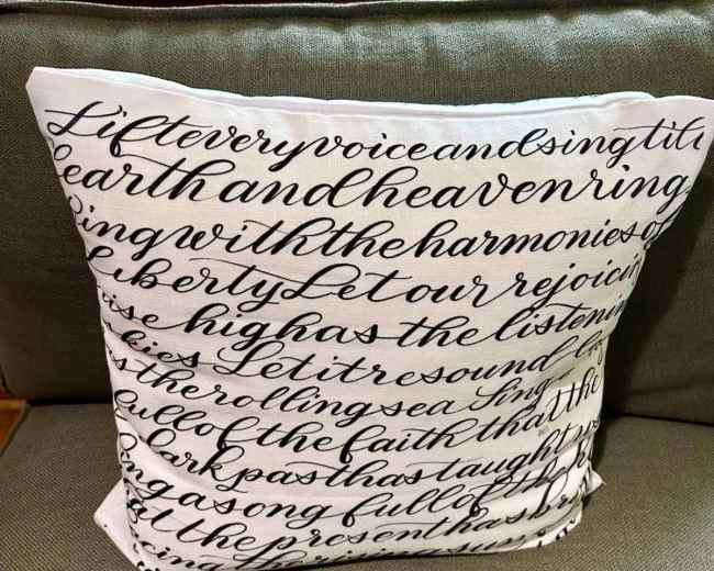 The image shows a decorative throw pillow with a text pattern featuring handwritten-style script.