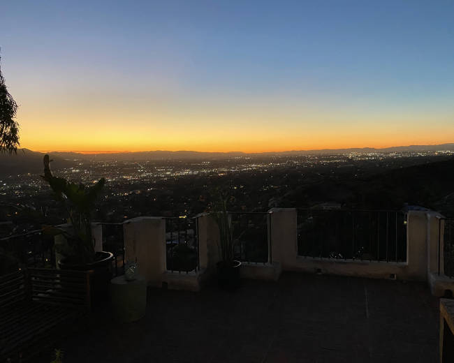 A sunset view over a city valley from a terrace, with distant lights scattered across the landscape.