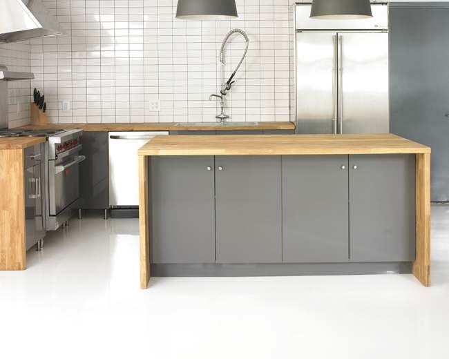 A modern kitchen features a stainless steel range, a wood-topped island, and gray cabinetry against a tiled wall.