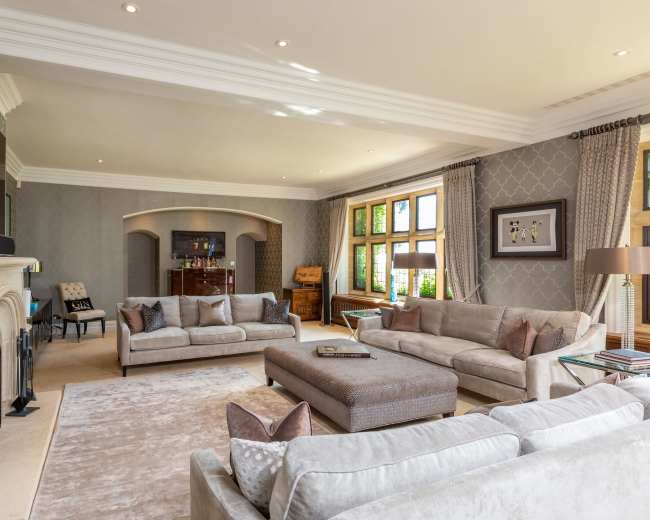 The living room features light-colored sofas arranged around a central coffee table, with large windows allowing natural light to illuminate the space.