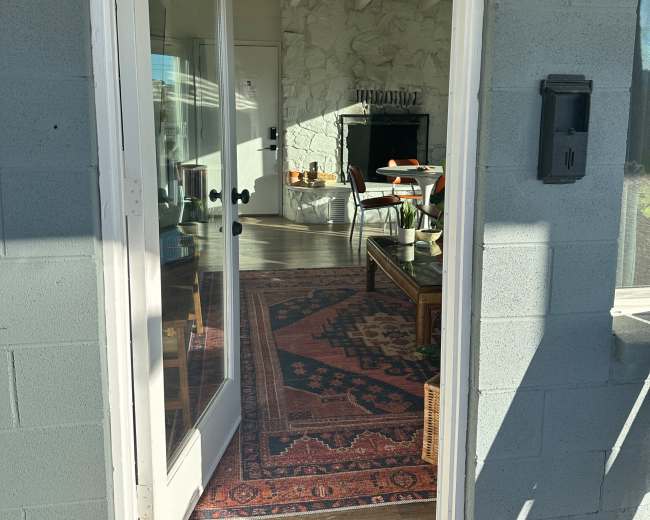 A partially open front door reveals a bright living room furnished with a rug, coffee table, and a fireplace.