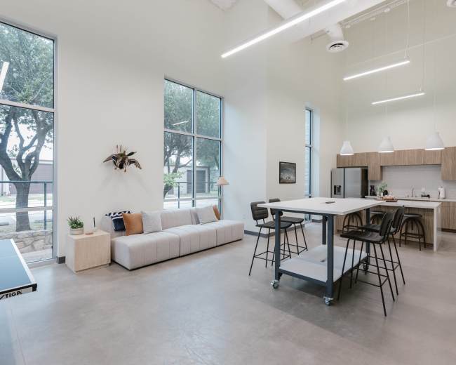 The image features a modern, open-plan living space with a sofa, dining table, and kitchen, illuminated by natural light from large windows.