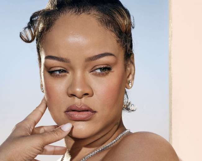 A woman with a sleek hairstyle poses outdoors, wearing a necklace and looking thoughtfully to the side.
