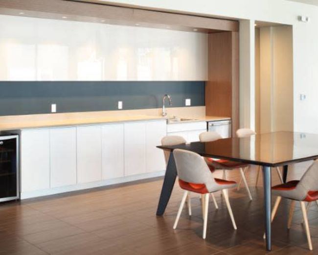 A modern kitchen features a sleek countertop with a sink, cabinets, and a dining table with chairs beside it.