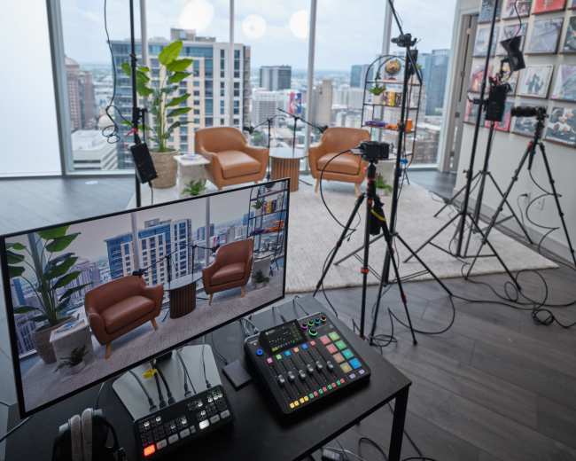 A well-equipped studio setup features two lighting setups, a control panel, and a large screen displaying a virtual background, all within a high-rise apartment.