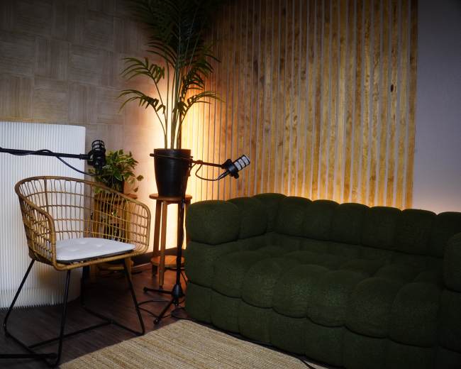 The image depicts a cozy corner of a room with a green sofa, a rattan chair, and plants, illuminated by warm lighting.