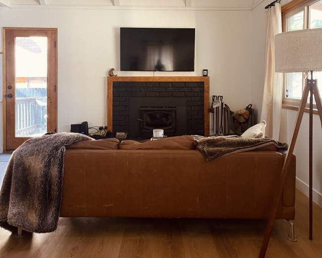 A cozy living room with a brown leather sofa facing a black fireplace and a television mounted on the wall.