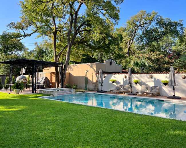 The image shows a landscaped backyard featuring a swimming pool surrounded by lounge chairs and a pergola.
