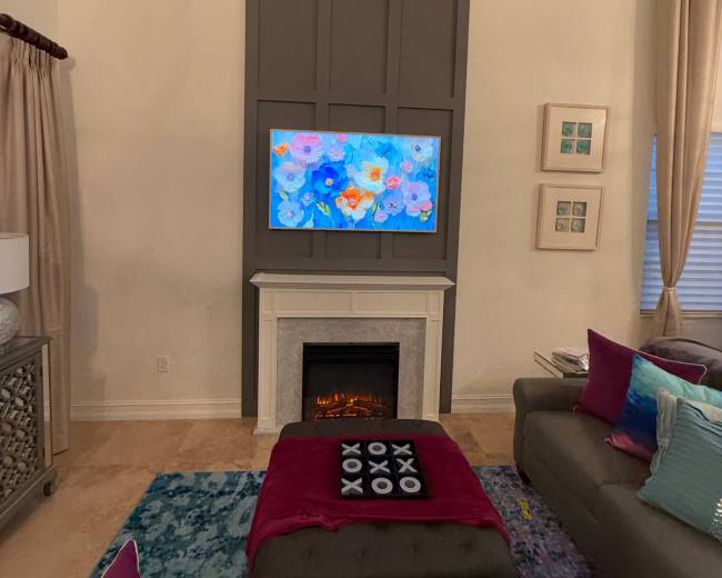 A television is mounted above a decorative fireplace in a modern living room, accented with colorful cushions and a patterned rug.
