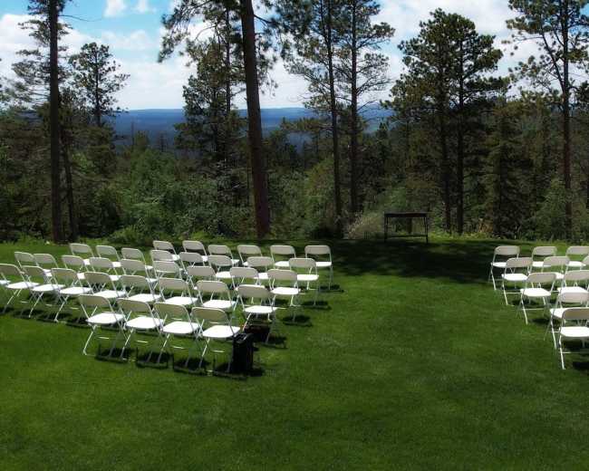 A set of white chairs is arranged in rows on a grassy area overlooking a forested landscape.
